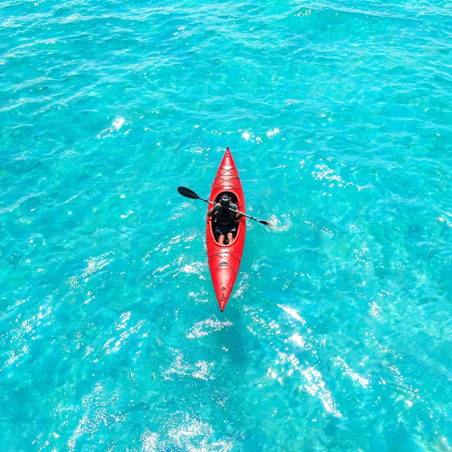 Original square aerial photo of a red kayak on turquoise water.